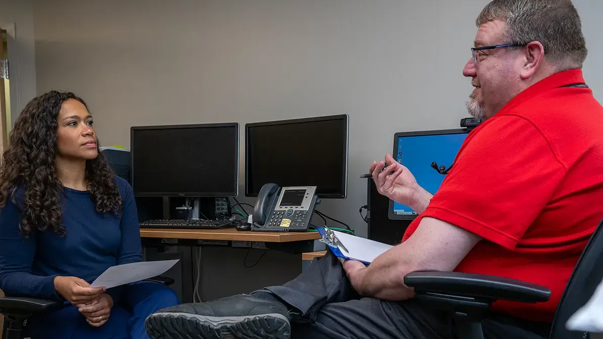 man talking with a woman in scrubs while holding a pen and clipboard